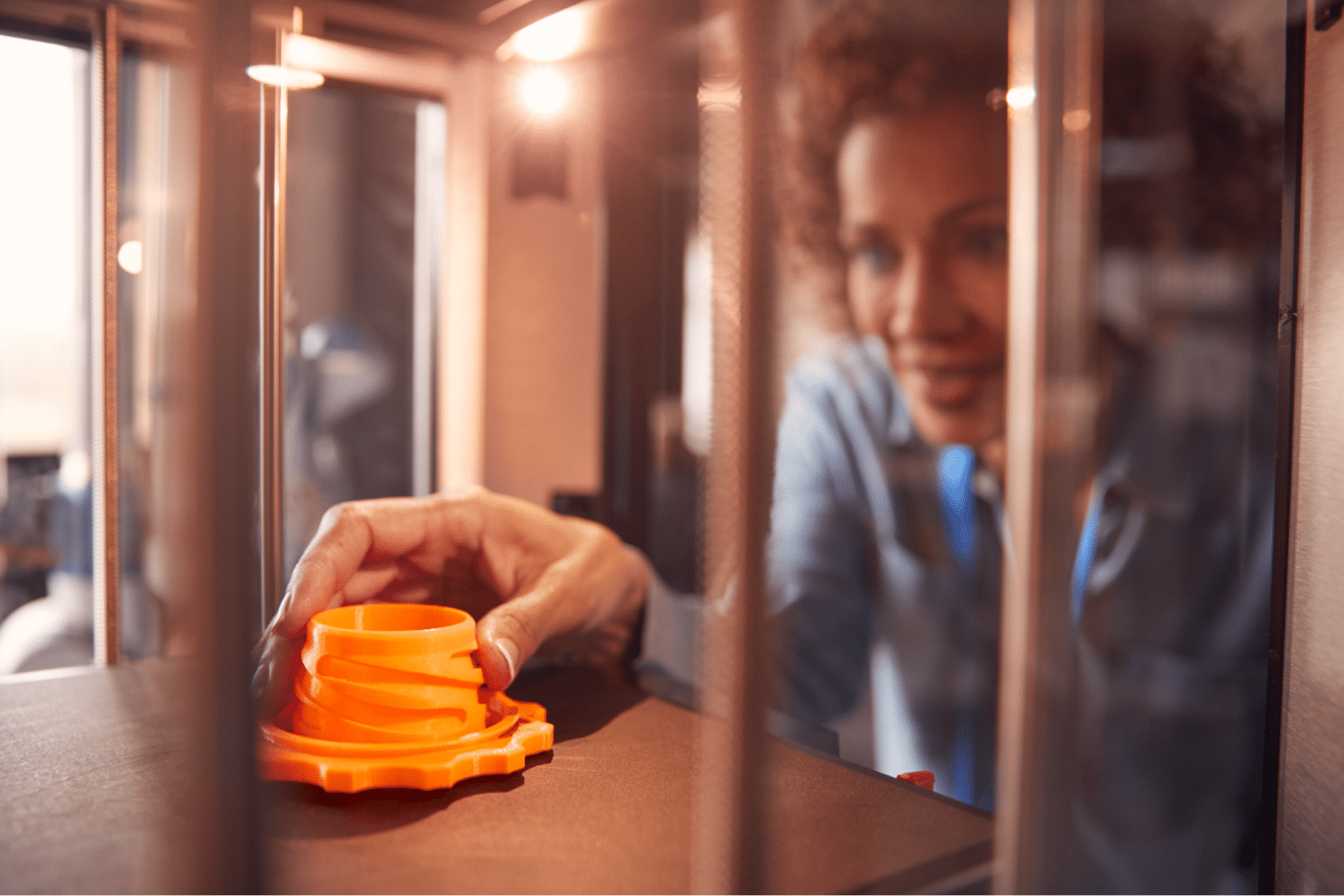 A designer examines a brightly colored 3D-printed object in a printer.