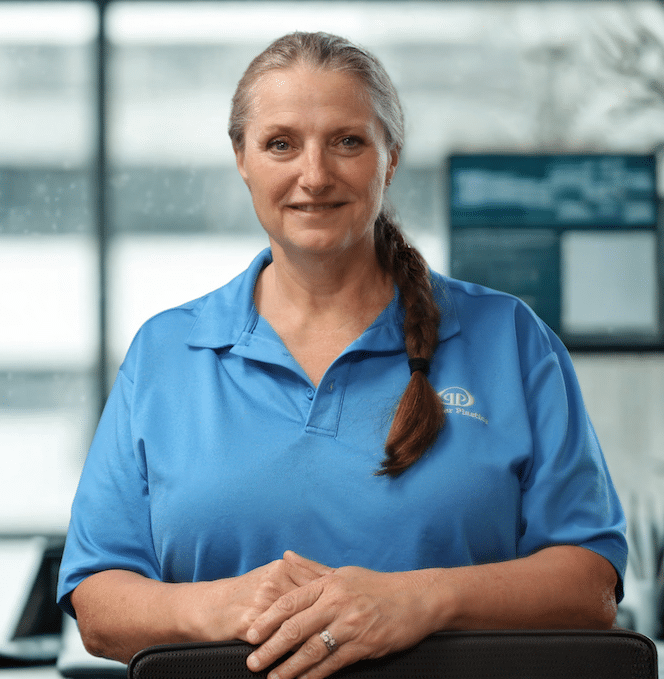 Professional woman in a blue shirt smiling, standing confidently in an office setting.