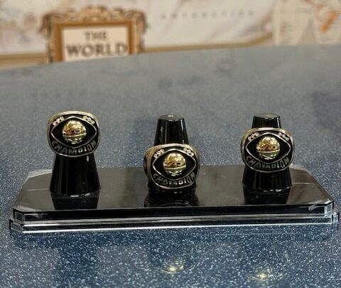 Display of three championship rings on a polished black stand.