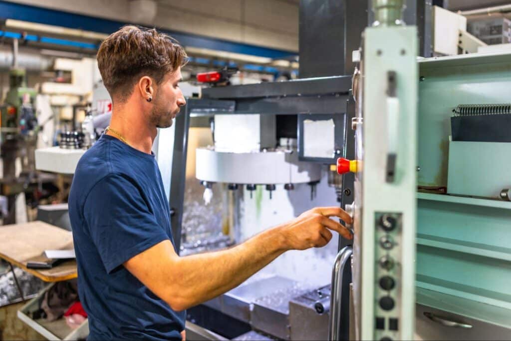 Skilled machine operator adjusting plastic injection molding equipment in a busy workshop environment.