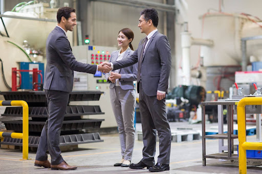 Business professionals shaking hands in a modern factory setting during a meeting.