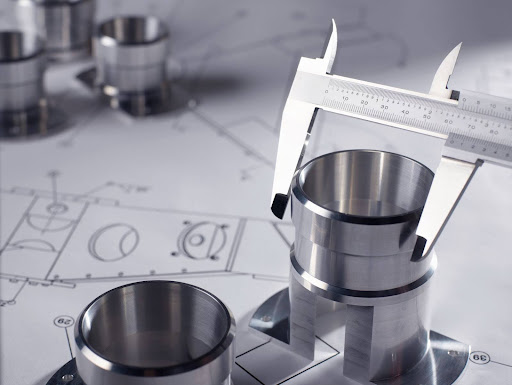 Precision measuring of metal parts with calipers on technical blueprints.