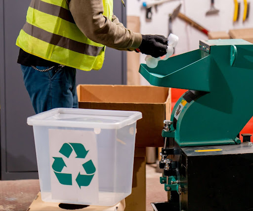 Worker managing recycling operations with a shredder and recycling bin.