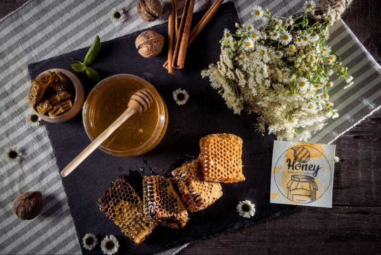 Honey, honeycomb, and flowers arranged on a rustic wooden surface create a vibrant presentation.