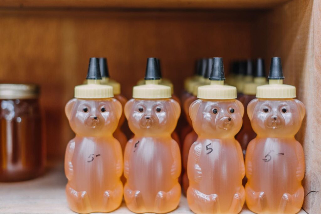Bottles of honey in bear shapes displayed on a wooden shelf.