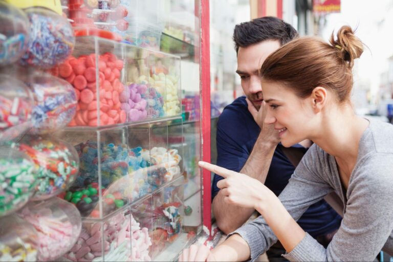 Couple admiring colorful candies in a charming candy store window display.
