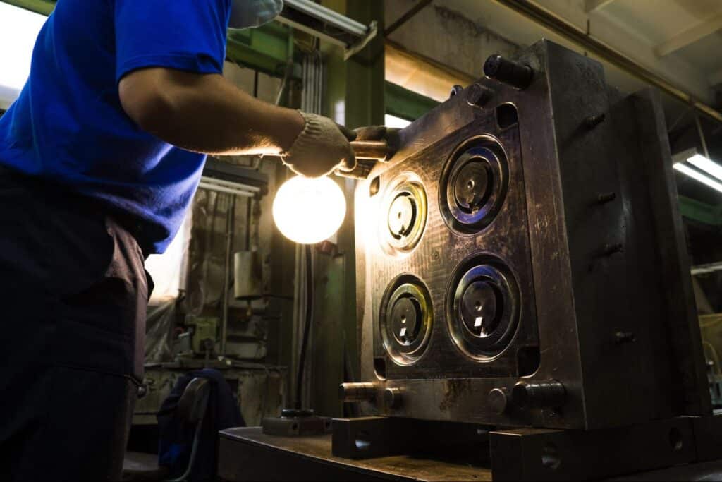 Worker inspecting injection mold for quality in precision engineering manufacturing.