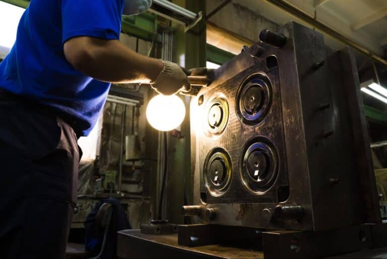 Worker inspecting injection mold for quality in precision engineering manufacturing.