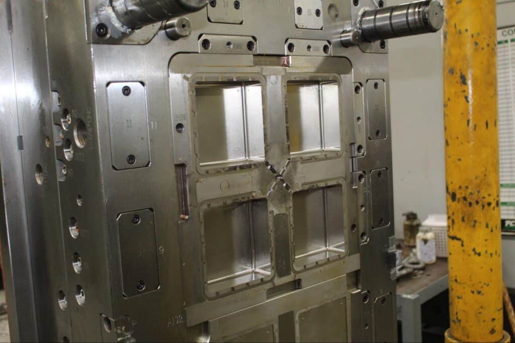 Industrial metal mold machine with steel panels and yellow support column.