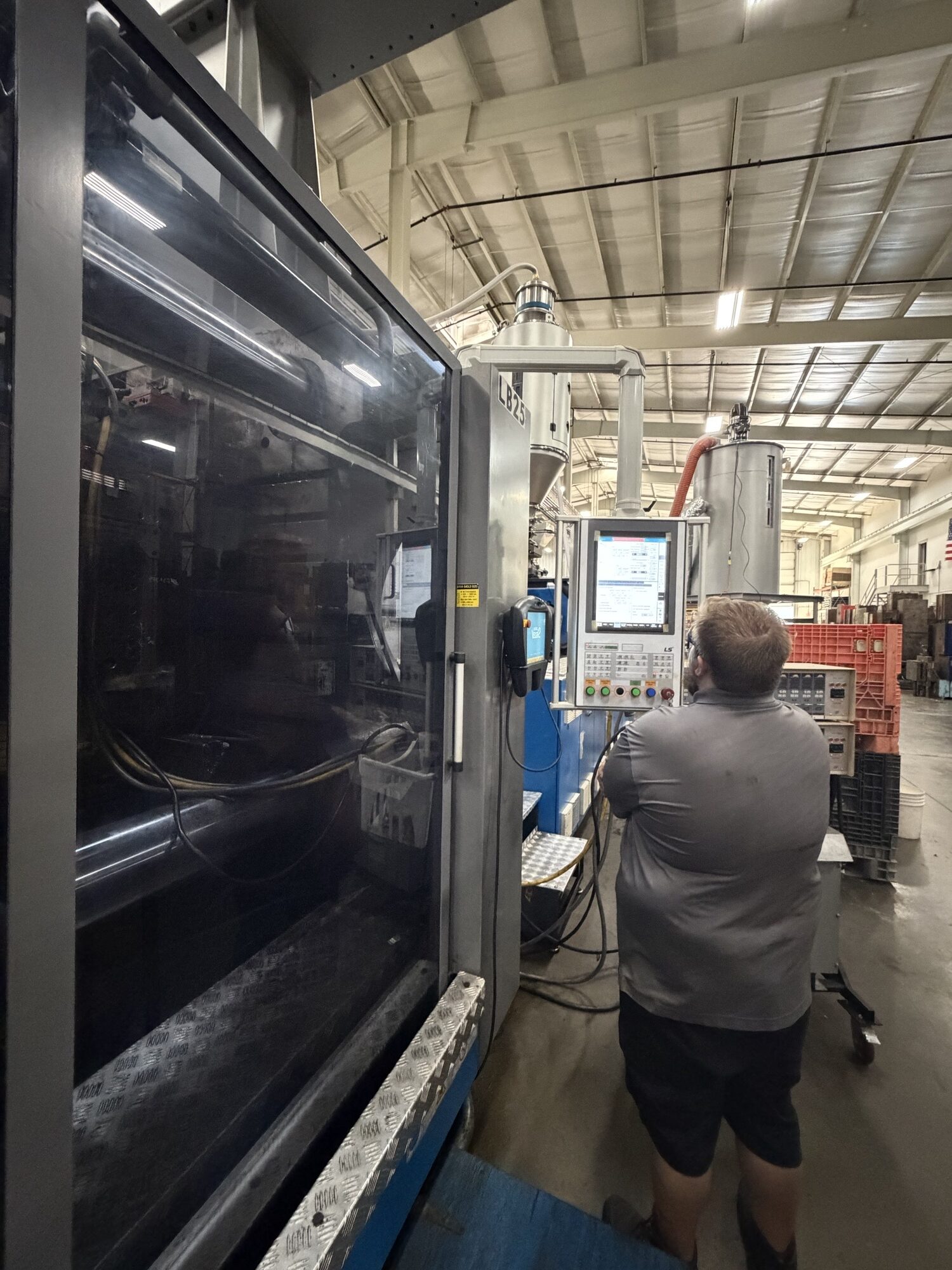 Machine operator at the control panel of an injection molding press on the production floor at Pioneer Plastics